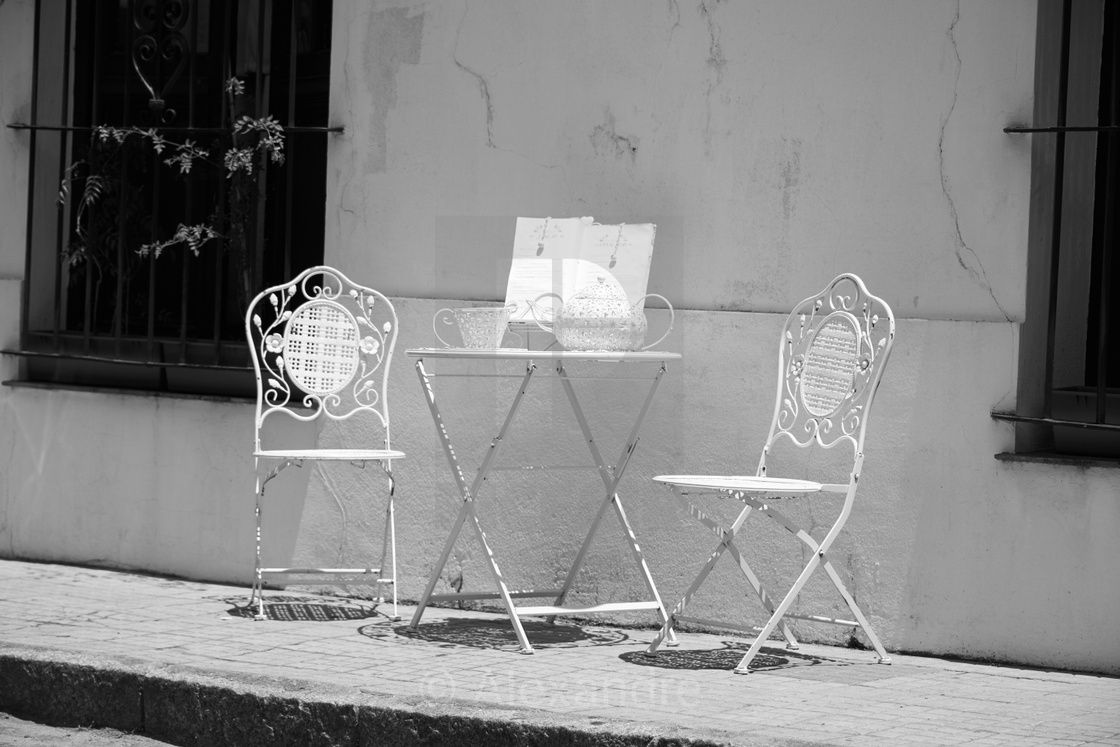 Mesa e duas cadeiras vazias numa rua, fotografia a preto e branco